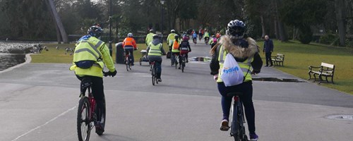 people riding bikes led by cycling uk. riding bikes through park facing away from camera